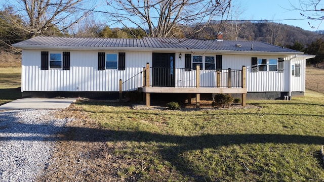 view of front of home with a chimney, metal roof, gravel driveway, a wooden deck, and a front lawn