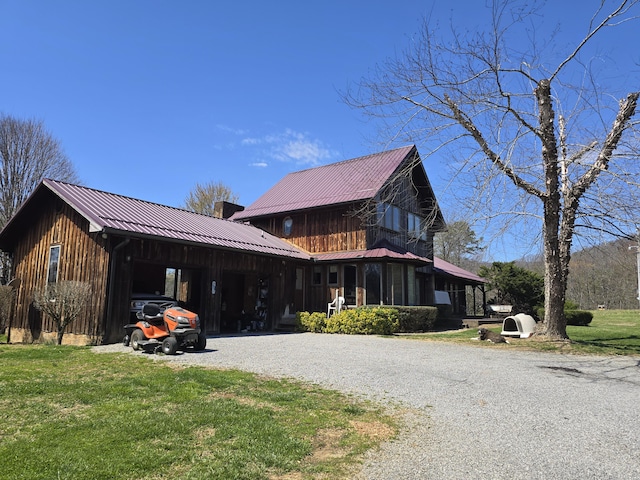 view of front facade with a front yard, metal roof, driveway, and a chimney