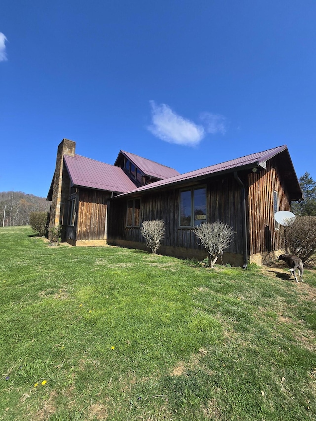 view of home's exterior featuring metal roof, board and batten siding, a chimney, and a lawn