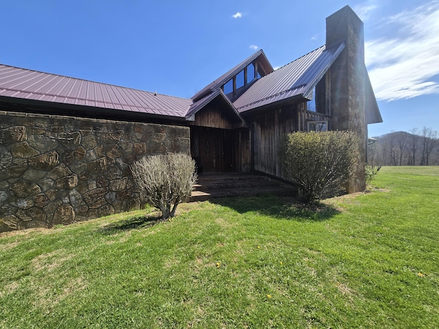 exterior space with a chimney, metal roof, stone siding, and a lawn
