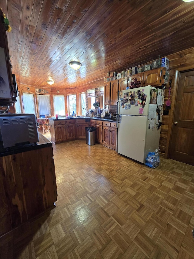 kitchen with a sink, a peninsula, freestanding refrigerator, dark countertops, and wooden ceiling