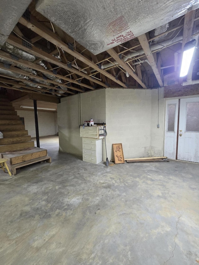 unfinished basement featuring stairs and concrete block wall