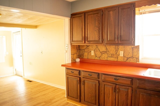 kitchen featuring baseboards, light wood-style flooring, light countertops, brown cabinets, and backsplash