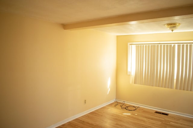 empty room featuring visible vents, baseboards, beam ceiling, and light wood finished floors