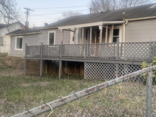 rear view of property with a shingled roof, a deck, and fence