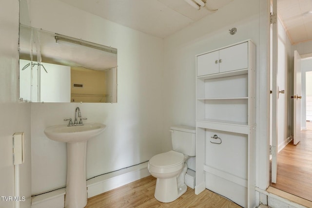 half bath with visible vents, toilet, a sink, wood finished floors, and baseboards