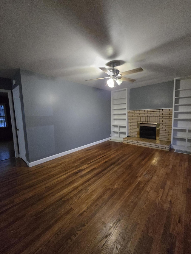 unfurnished living room with dark wood-type flooring, a brick fireplace, built in shelves, ceiling fan, and a textured ceiling