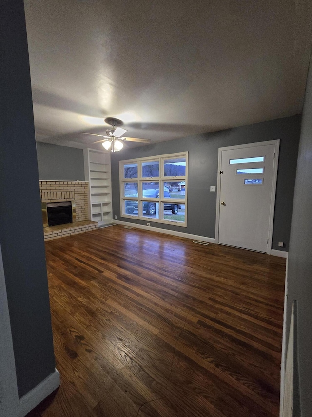 unfurnished living room with ceiling fan, dark hardwood / wood-style flooring, built in features, and a fireplace