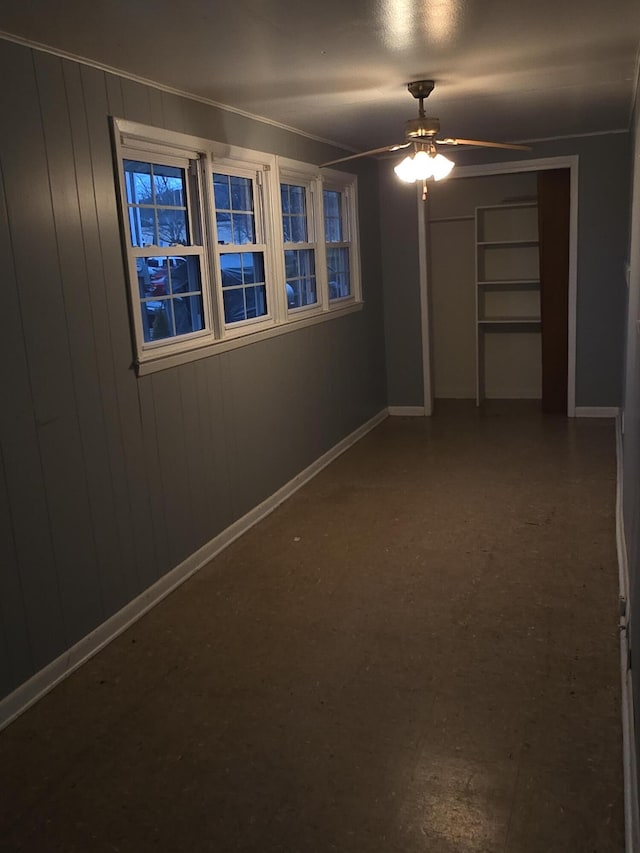 empty room with wood walls, ceiling fan, and ornamental molding