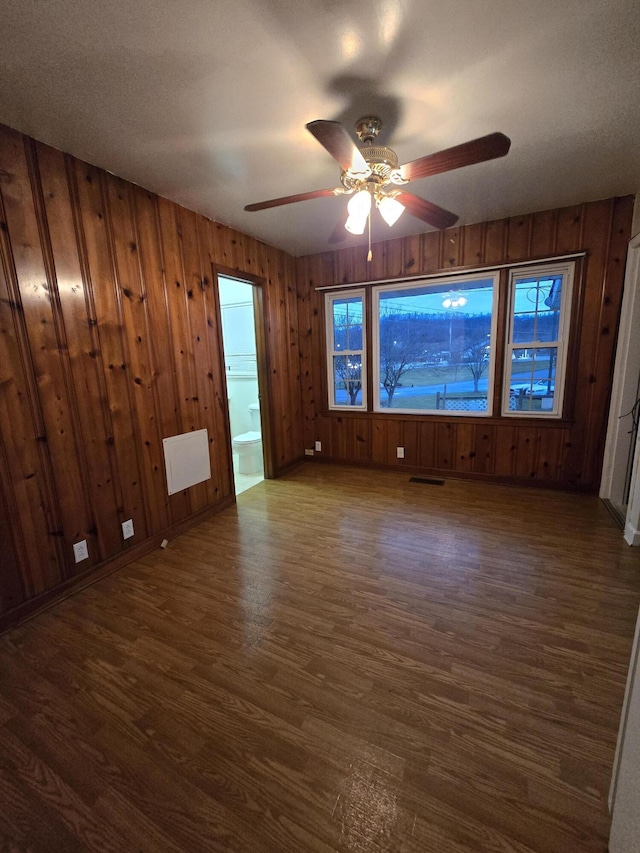 empty room featuring ceiling fan, wooden walls, and dark hardwood / wood-style floors