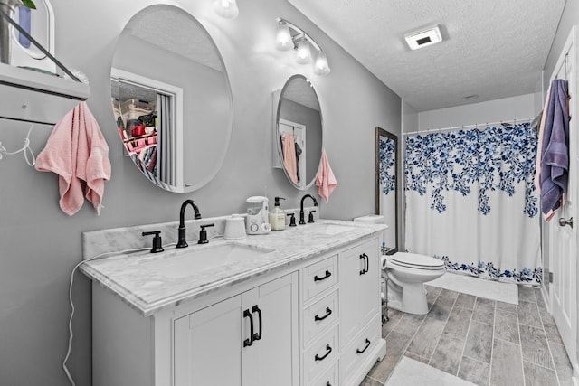 bathroom with a textured ceiling, toilet, vanity, and curtained shower