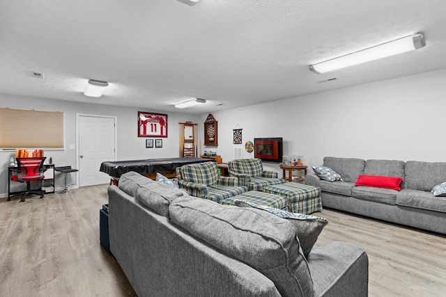 living room featuring pool table, light wood-type flooring, and a textured ceiling