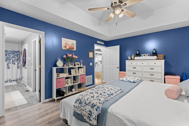 bedroom with a raised ceiling, light wood-type flooring, ceiling fan, and a textured ceiling