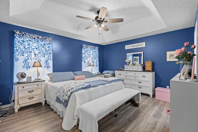 bedroom with a textured ceiling, dark hardwood / wood-style floors, ceiling fan, and a raised ceiling