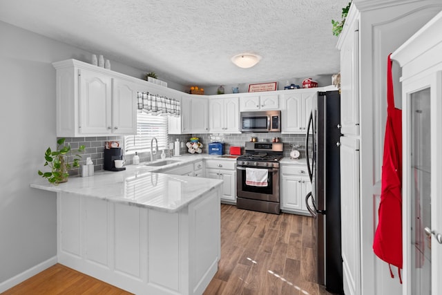 kitchen with appliances with stainless steel finishes, sink, kitchen peninsula, white cabinets, and hardwood / wood-style flooring