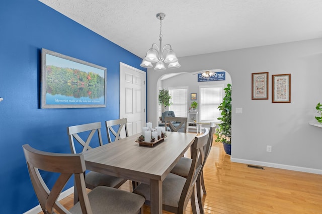 dining space with light wood-type flooring, a textured ceiling, and a notable chandelier