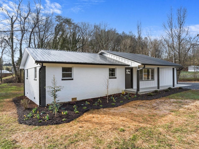 view of front of home featuring metal roof, crawl space, a front lawn, a porch, and brick siding