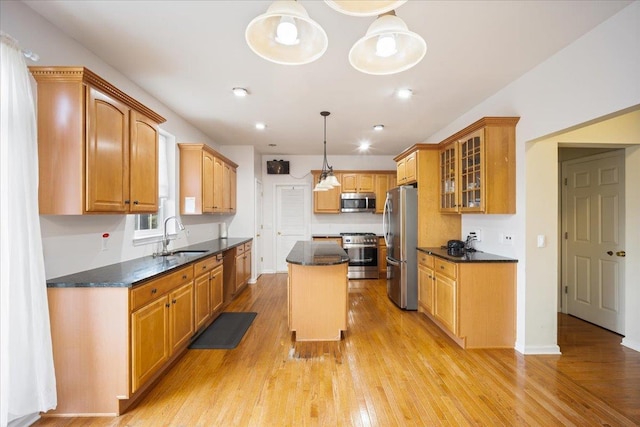 kitchen with appliances with stainless steel finishes, sink, light hardwood / wood-style flooring, a kitchen island, and hanging light fixtures