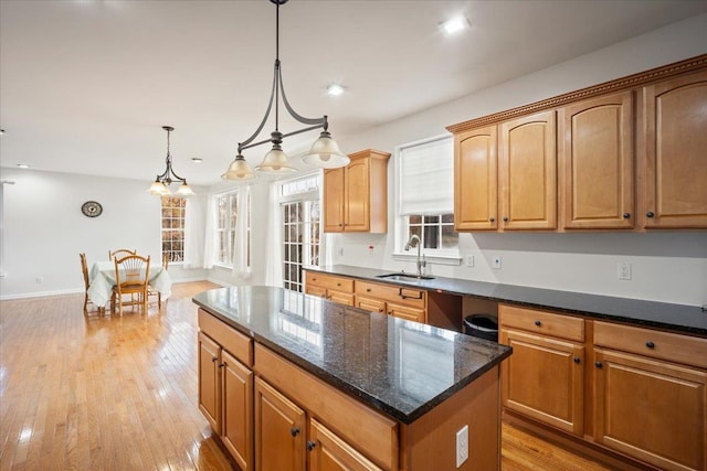 kitchen with light wood-type flooring, sink, pendant lighting, dark stone countertops, and a center island