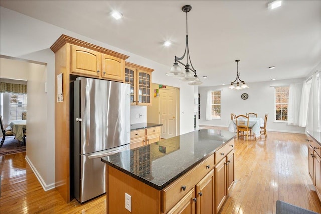 kitchen with a healthy amount of sunlight, a kitchen island, light wood-type flooring, and stainless steel refrigerator