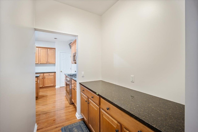 kitchen featuring light wood-type flooring, stainless steel appliances, and dark stone counters