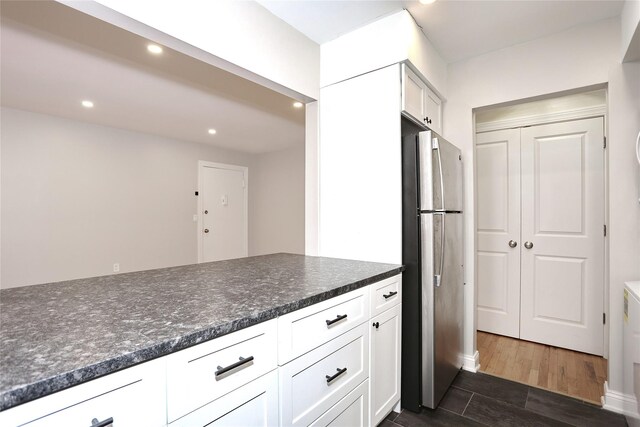 kitchen with white cabinets, dark hardwood / wood-style floors, dark stone countertops, and stainless steel refrigerator