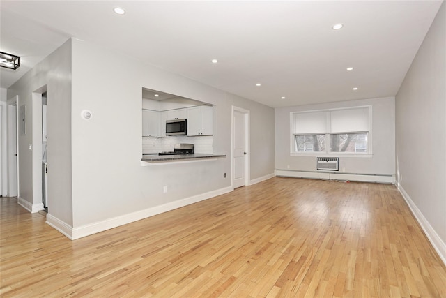 unfurnished living room with baseboard heating, a wall unit AC, and light hardwood / wood-style floors