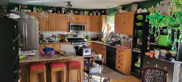 kitchen with light stone countertops, a breakfast bar, stainless steel appliances, pendant lighting, and light hardwood / wood-style flooring