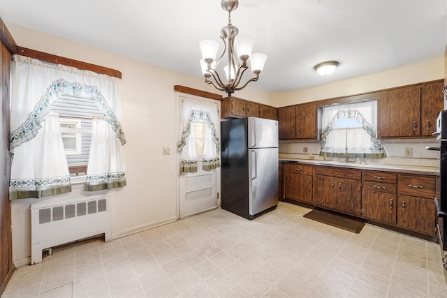 kitchen with radiator, sink, a notable chandelier, stainless steel fridge, and decorative light fixtures