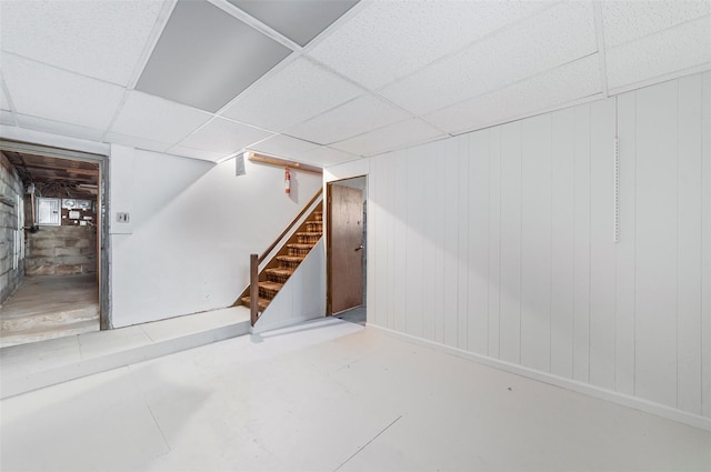 basement featuring a paneled ceiling and wooden walls