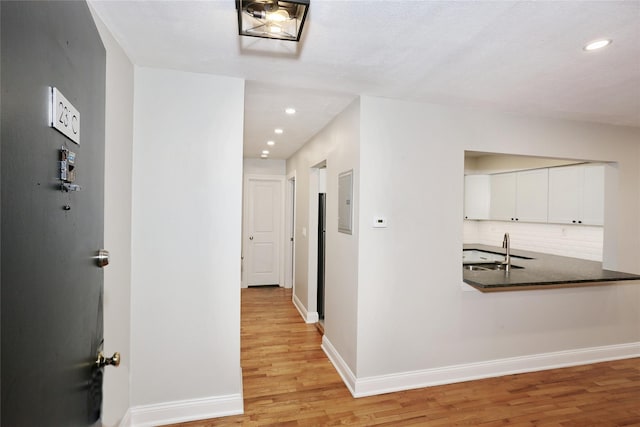 hall with electric panel, light hardwood / wood-style flooring, and sink