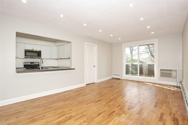 unfurnished living room with light hardwood / wood-style flooring, a wall mounted AC, a baseboard heating unit, and sink