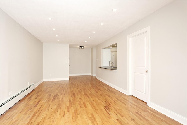 unfurnished room with a baseboard radiator, light hardwood / wood-style floors, and sink