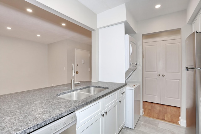 kitchen with light wood-type flooring, sink, white cabinetry, stacked washer / drying machine, and stainless steel refrigerator