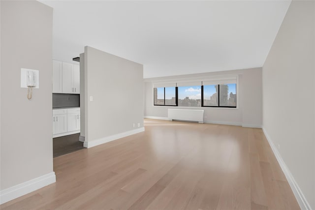 unfurnished living room featuring radiator and light wood-type flooring