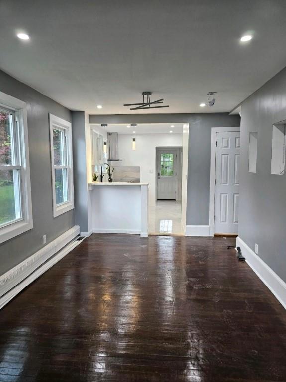 unfurnished living room with baseboard heating, ceiling fan, and wood-type flooring