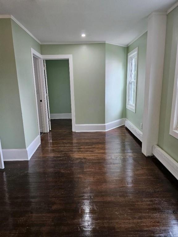 empty room featuring a baseboard heating unit, ornamental molding, and dark wood-type flooring