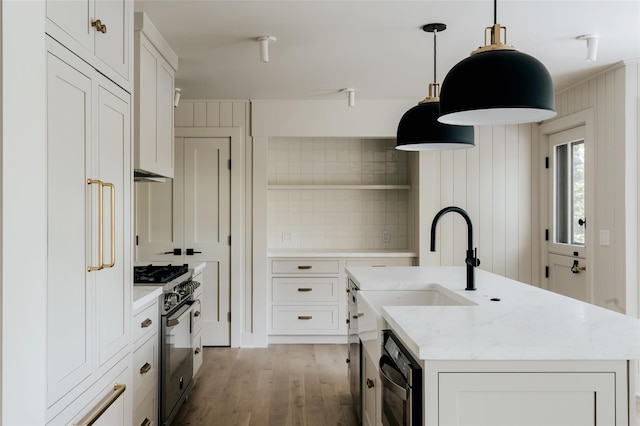 kitchen with light wood-type flooring, backsplash, stainless steel range, a kitchen island with sink, and white cabinetry