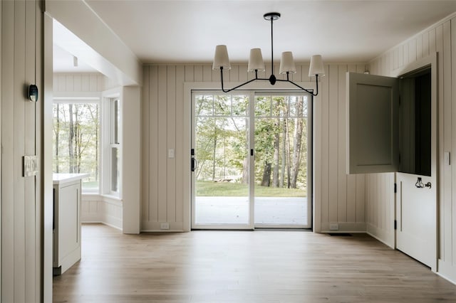 doorway with light wood-type flooring, an inviting chandelier, and wood walls