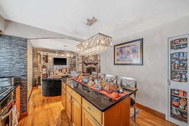 kitchen with light wood-type flooring, a fireplace, a kitchen island, hanging light fixtures, and a breakfast bar area