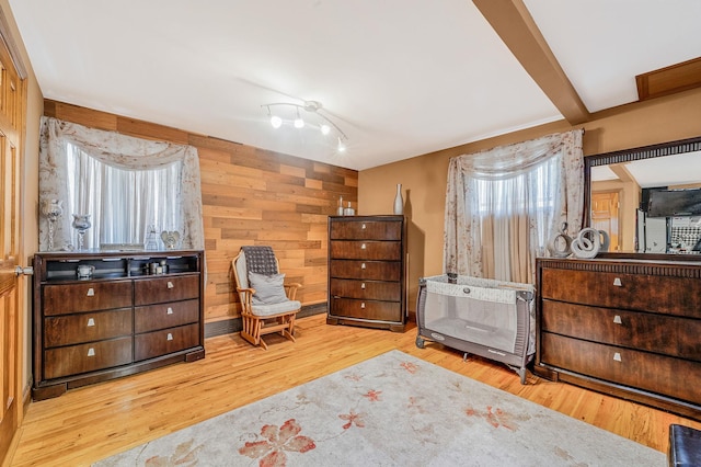 bedroom with beam ceiling, light hardwood / wood-style flooring, wooden walls, and multiple windows