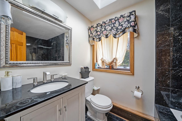 bathroom with a tile shower, vanity, a skylight, and toilet