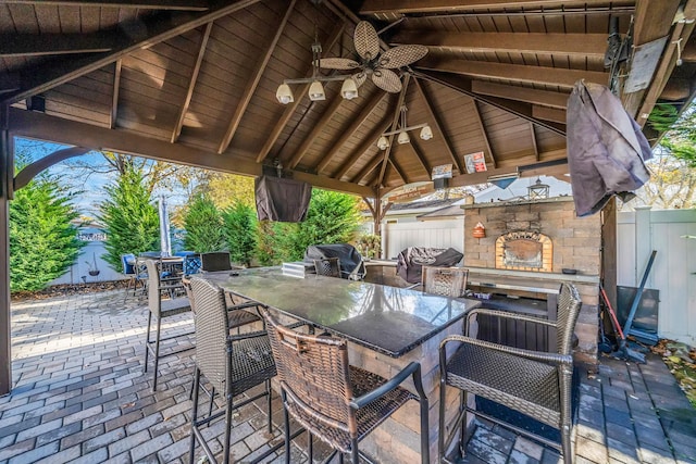 view of patio / terrace featuring ceiling fan, a grill, an outdoor bar, an outdoor stone fireplace, and a gazebo