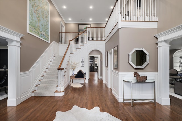 foyer featuring a high ceiling, dark hardwood / wood-style floors, ornate columns, and ornamental molding