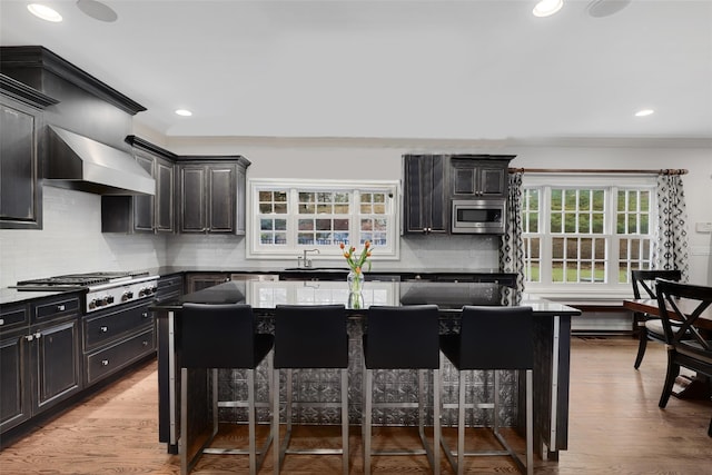 kitchen featuring a healthy amount of sunlight, wall chimney range hood, a breakfast bar area, and appliances with stainless steel finishes