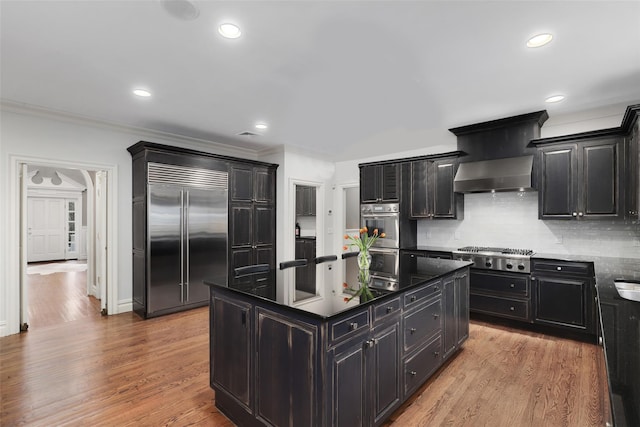 kitchen featuring light wood-type flooring, tasteful backsplash, stainless steel appliances, wall chimney range hood, and a kitchen island