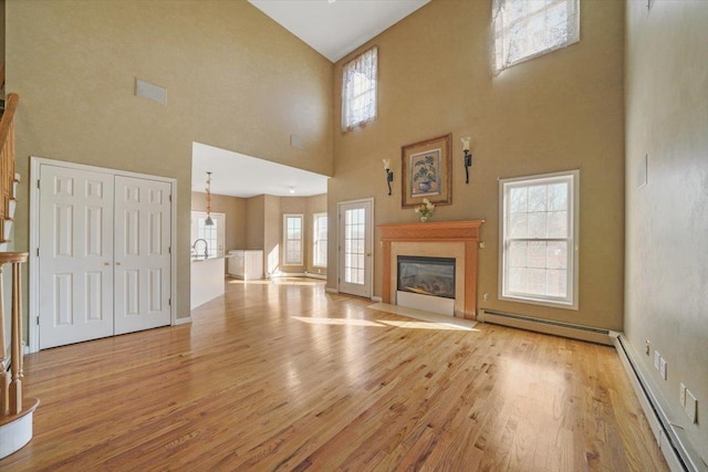 unfurnished living room with a towering ceiling, light hardwood / wood-style floors, and a baseboard radiator