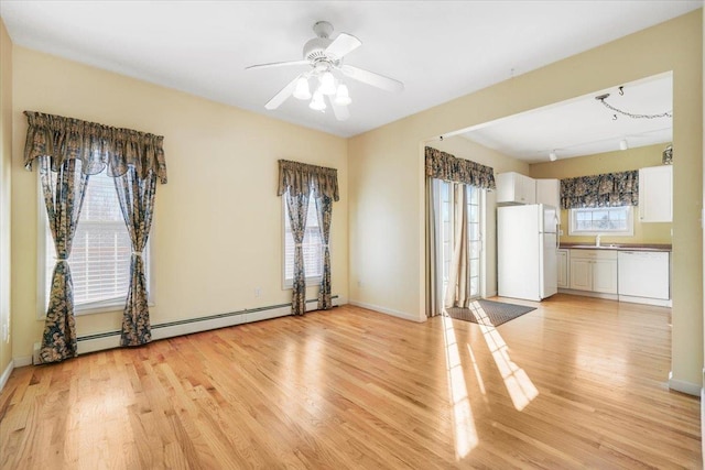 interior space with light wood-type flooring, a baseboard radiator, ceiling fan, and sink