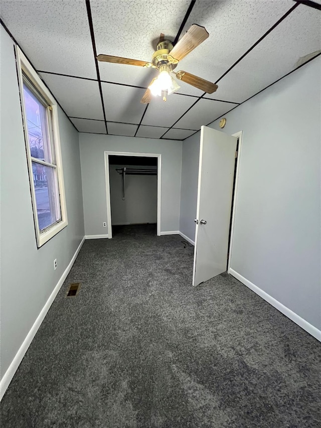 unfurnished bedroom featuring dark colored carpet, a paneled ceiling, a closet, and ceiling fan