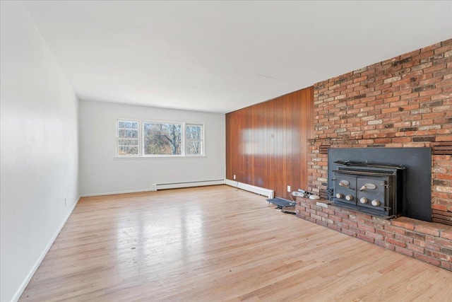 unfurnished living room with a wood stove, wood walls, a baseboard radiator, and light wood-type flooring